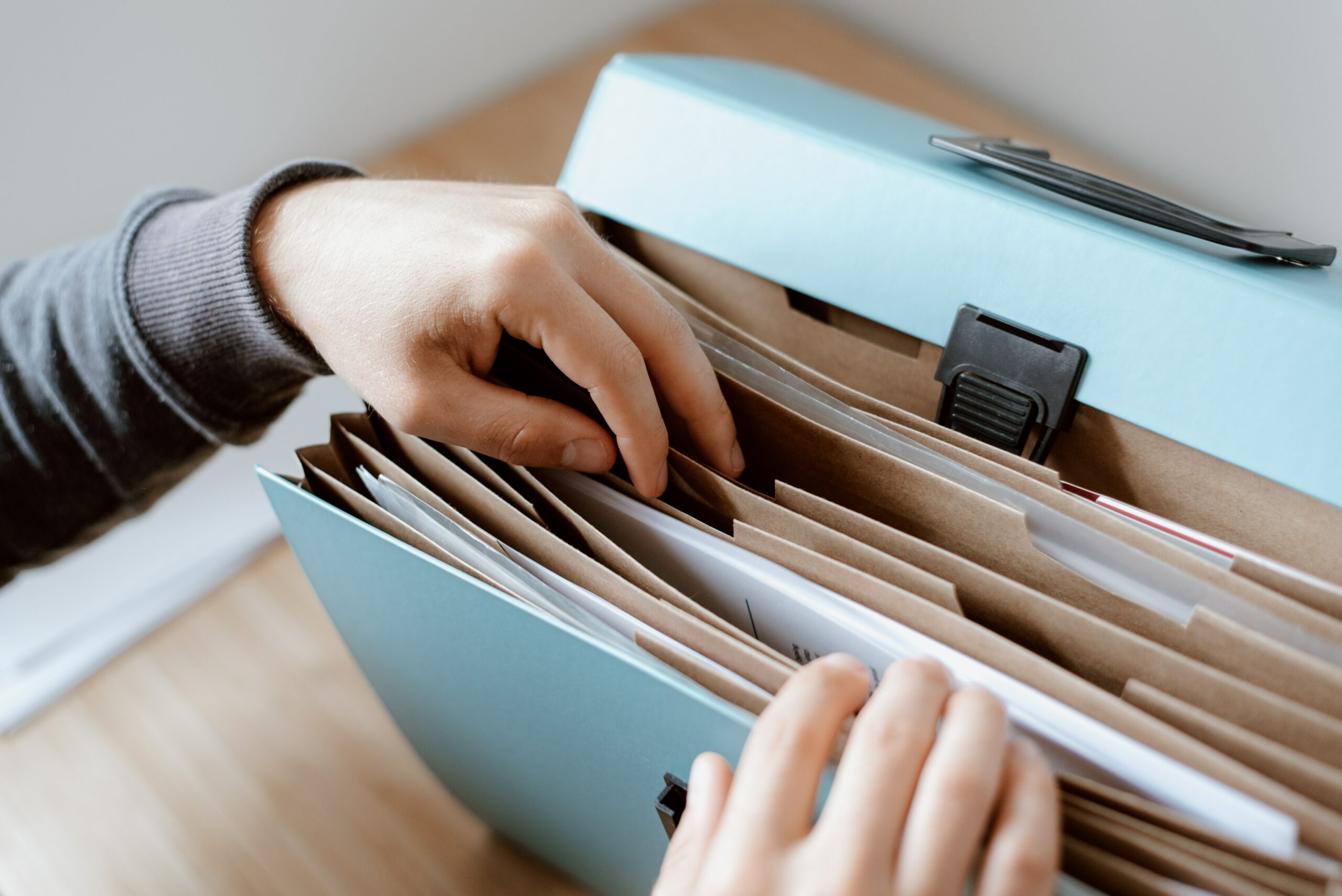 Photo of hands flipping through file folders inside of a blue file case. Photo by Anete Lusina: https://www.pexels.com/photo/person-choosing-document-in-folder-4792285/