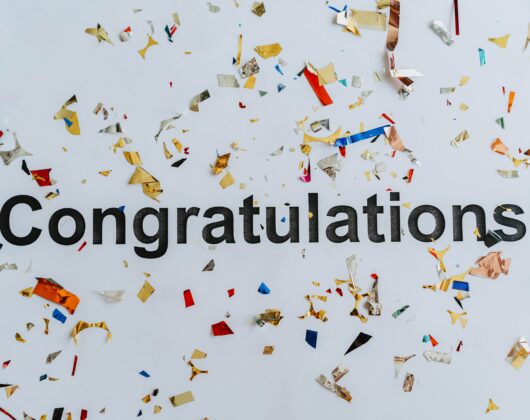 The world congratulations in bold black font in the center of a white background with multi colored confetti scattered around. Photo by olia danilevich: https://www.pexels.com/photo/congratulations-text-on-white-surface-with-confetti-8127309/