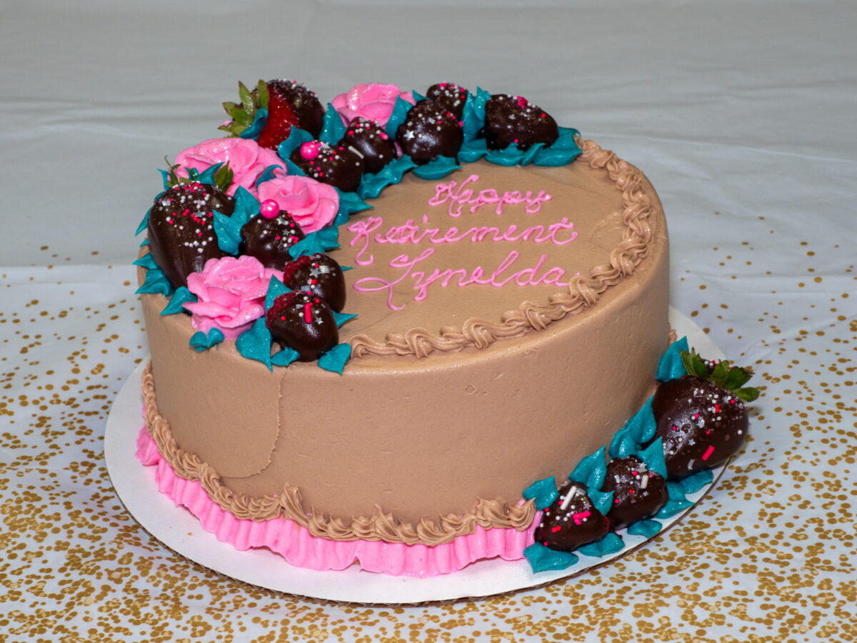 Chocolate cake with brown and pink frosting and chocolate covered strawberries and raspberries with the message: "Happy Retirement Lynelda" Copyright 2023, Stroud National Agency, Inc. All Rights Reserved.