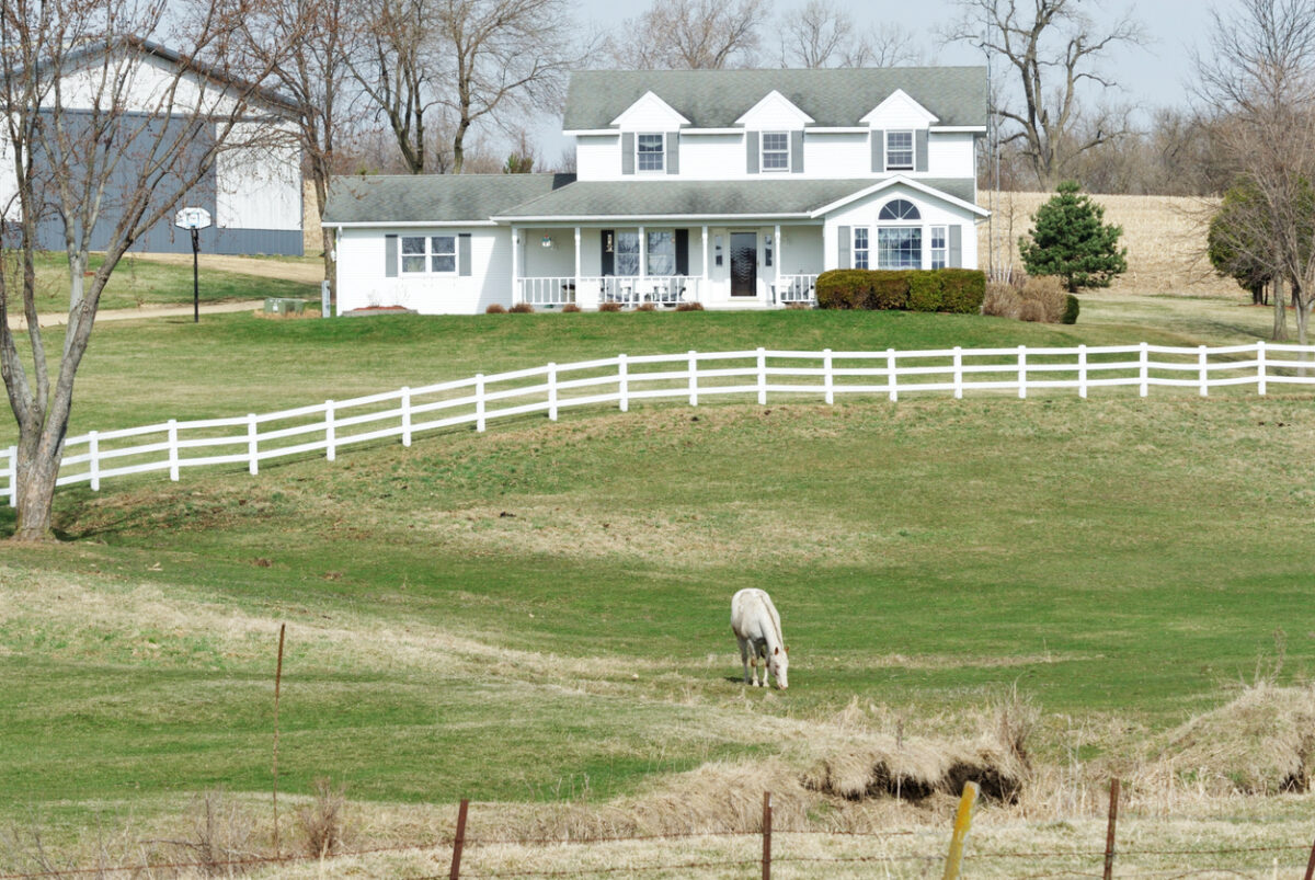 White farmhouse with fenced pasture and grazing horse on a hobby farm property, ideal for hobby farm insurance coverage.