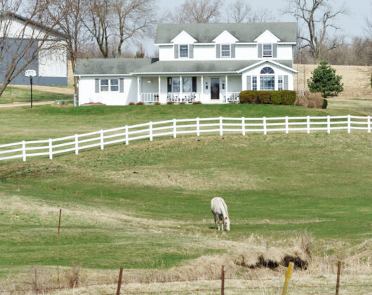 White farmhouse with fenced pasture and grazing horse on a hobby farm property, ideal for hobby farm insurance coverage.